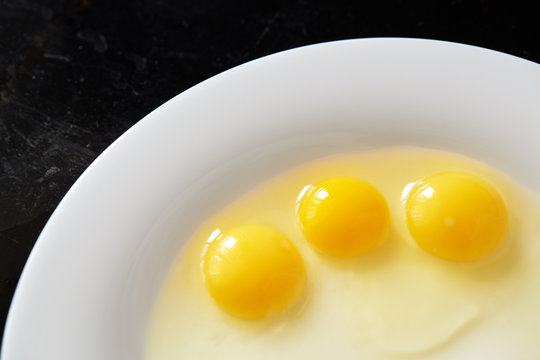 Three broken quail eggs in white plate on black background