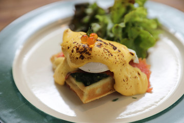 Breakfast food egg benedict , poached egg with yellow sauce with waffle and smoked salmon on wood background