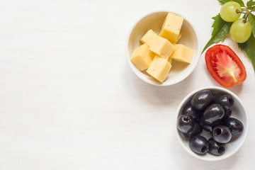 Ingredients for snacks, cheese with olives and tomato, grape on a white table with copy space.