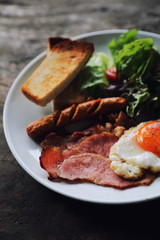 English breakfast  fried egg, ham,sausage, bacon,salad and toast on wood background in mystic light