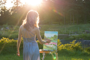 Naklejka premium The painter paints oil paintings in the garden at sunset
