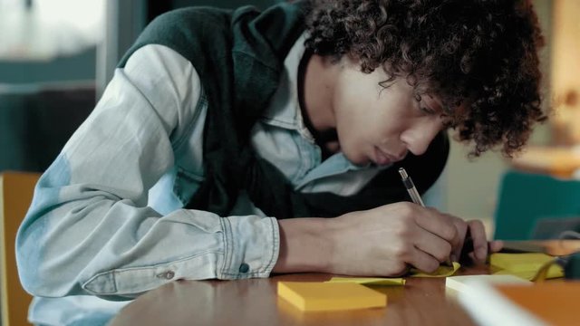 Close up creative young african male with curly hair diligently writes notes on sticky multi colored stickers preparation discussing and planning strategy of business start up project on team meeting