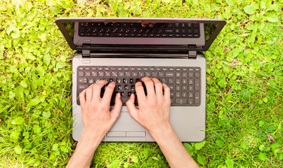 Laptop on the grass. Work on a computer in the nature. Human hands on the keyboard
