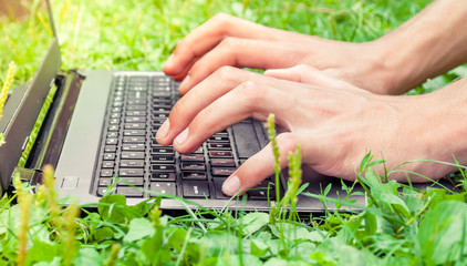 Human hands typing on laptop keyboard with green nature background , outdoors lifestyle concept