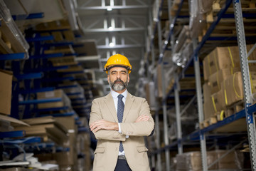Portrait of senior businessman in suit with helmet in a warehouse