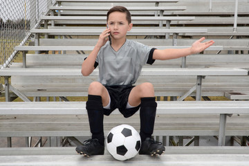 Male child soccer player talking on phone while waiting for ride