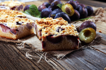Rustic plum cake on wooden background with plums around.