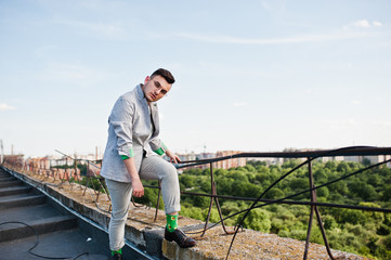 Dreamer stylish macho man in gray suit and glasses posed on the roof.