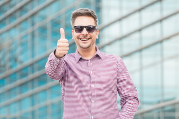 Happy executive in sunglasses showing thumbs up outdoors.