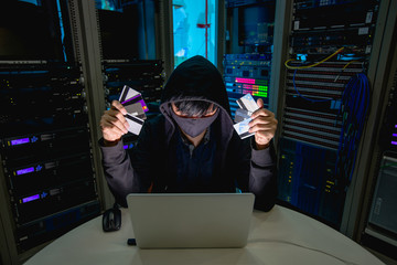 Hacker holding credit card and using computer laptop for credit card hacking.