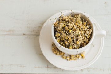 Dried chamomile flowers. Herbal tea in a white cup, top view, wooden background