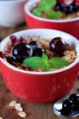 Crumble with berries in portion ceramic bowls topped with black currant and mint