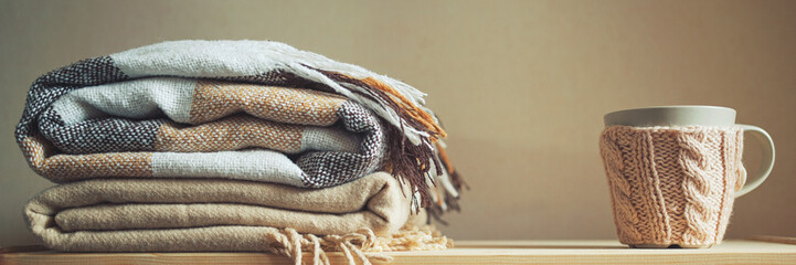 stack of beige checkered wool blankets and cup on a wooden chest. autumn - winter concept of home...