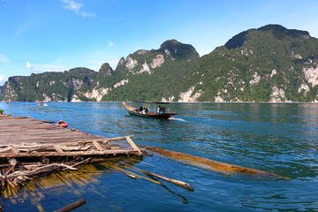 Khaosok or Ratchaprapa Dam in Southern of Thailand. The mountain and blue sky in background with bamboo raft and a tourist boat in the clear water. This photo took in July 2016.