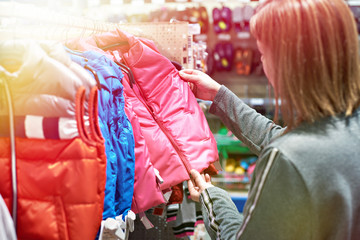 Buyer woman chooses kid jacket clothes in store