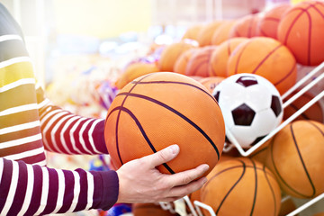 Buyer hands with football and basketball in sports shop