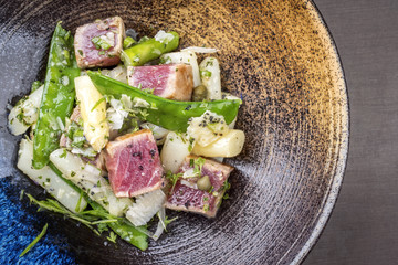 Modern fried tuna fish tataki filet salad with white asparagus sugar snaps and parmesan cheese as top view on a plate