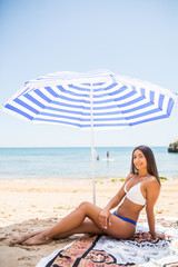 Smiling beautiful latin woman sunbathing on a beach under umbrella on the sea beach
