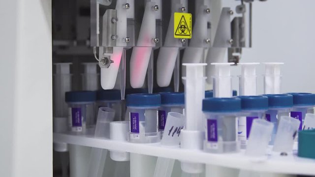 Close-up in the medical laboratory, the robot pierces a jar of liquid with a needle and pours it into a tube for further analysis by the doctor