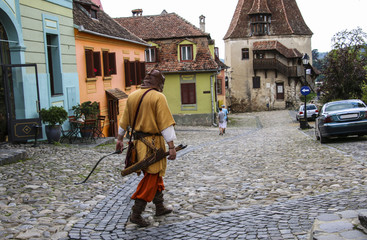 Man dressed in the costume of a medieval archer goes on one of the streets with colorful houses in Sighisoara, Romania.