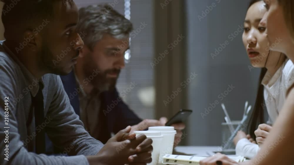 Poster handheld shot of four colleagues of diverse ethnicities sitting at desk in office and discussing pro