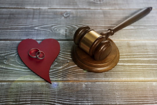 a pair of wedding rings on a wooden red heart shape, a judge hammer on a wooden background. family law. divorce and conflicts.