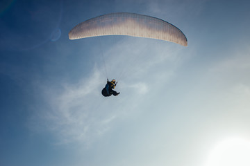 A man is flying on a paraglider in a blue sky