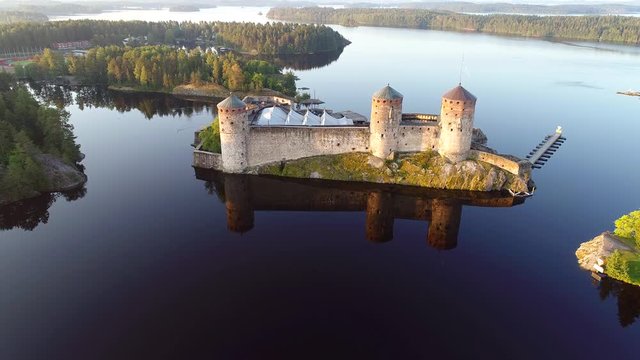 Olavinlinna fortress in the landscape of lake Saimaa. July morning. Savonlinna, Finland (aerial video)