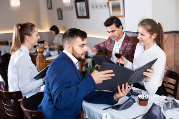 Сheerful friends choosing dishes out of menu card in restaurant