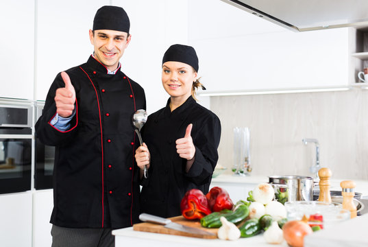 Man and woman young cooks in uniform showing thumbs up
