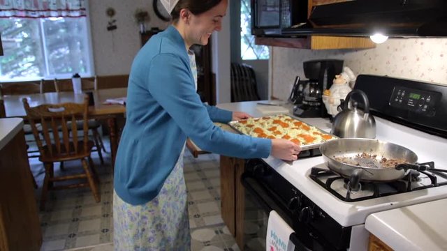 A Mennonite woman smiles as she puts a homemade pizza in the oven in slow motion.