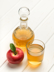 Bottle and a glass filled with apple cider vinegar on a white wooden background