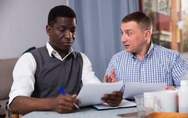Interracial men working in home interior with documents