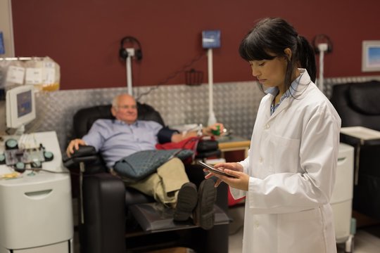 Physician using digital tablet while senior man donating blood