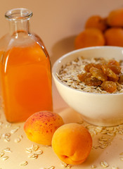 Healthy breakfast. White plate of oatmeal with dried apricots, a glass of an apricot juice and fresh apricots on a white table.
