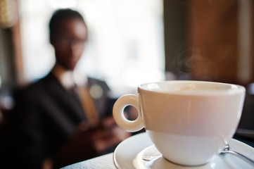 Close-up cup of hot coffee against african american businessman.