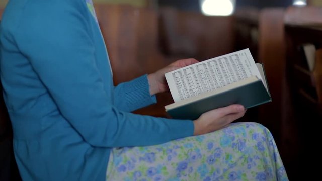 A Mennonite woman sits in an empty church and flips through the pages of a hymnal in slow motion.