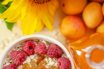 Healthy breakfast. White plate of oatmeal with dried apricots and raspberries, a glass of an apricot juice and fresh apricots on a white table.