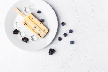 Homemade frozen ice cream popsicles from fruits and berries on table whith flowers and ingridients, top view