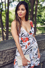 Fototapeta premium Beautiful Woman Stands Next to a Stone Wall in an Urban Park