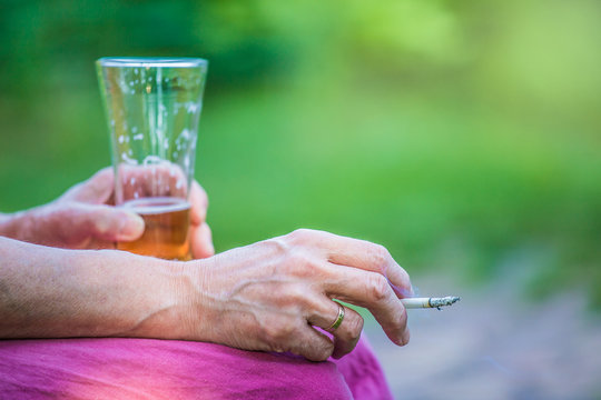 eine Frau mittleren Alters trinkt ein Bier und raucht eine Zigarette