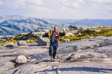 Fototapeta premium Portrait of a extreme plan travel for the handsome old man on the stone of the kjerag in the mountains kjeragbolten of Norway, selfie on a smartphone holding in your freedom hand