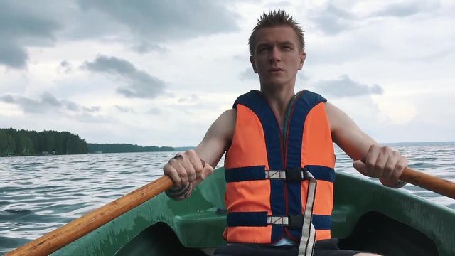 A young man in a boat rowing wooden oars on the water. Life jacket on the body of a man.