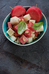 Summer salad with fresh watermelon and melon cubes and addition of nuts, vertical shot over grey stone background with space