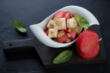 Black wooden serving board with a bowl of watermelon and melon fruit salad, studio shot on a black stone background