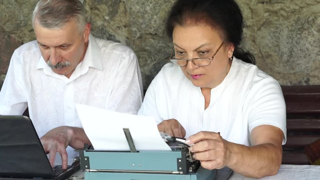 mature man work with notebook and woman typing on typewriter using magnifying glass. competitive typing. old vintage obsolete versus new modern technologies
