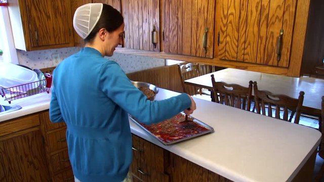 A Mennonite woman talks as she prepares food in her home.
