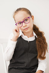 Portrait of a cute school girl in academic clothes, Wearing white shirt and grey dress. Girl with purple eye glasses. Educational concept. Isolated. Back to school.