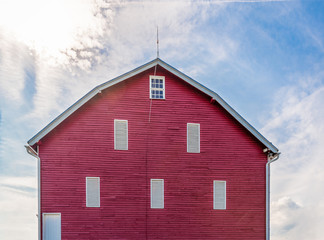 A bright red barn on farmland in western Virginia beneath a bright sun in a partly cloudy blue summer sky