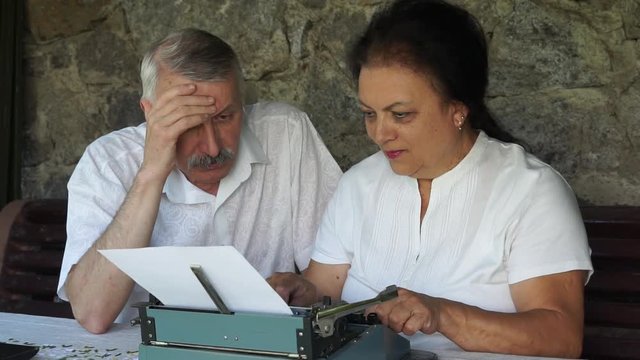 senior couple writing traditional mail by typewriter. woman typing and man sitting and thinking about story